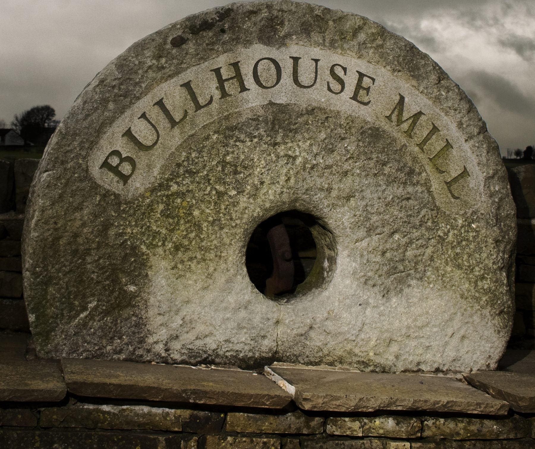 An old millstone carved with the words Bullhouse Mill, set on a dry-stone wall